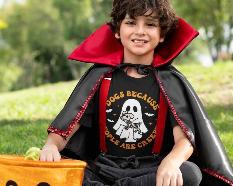 May include: A child dressed as a vampire for Halloween is wearing a black t-shirt with a white ghost and a dog skeleton inside. The shirt says "Dogs Because People Are Creepy".