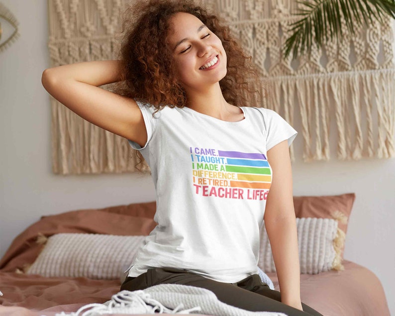 Puede incluir: Camiseta blanca con el texto "I CAME, I TAUGHT, I MADE A DIFFERENCE, I RETIRED, TEACHER LIFE" en colores arco&iacute;ris. La camiseta tiene cuello redondo y mangas cortas. El texto est&aacute; dispuesto en l&iacute;nea horizontal.