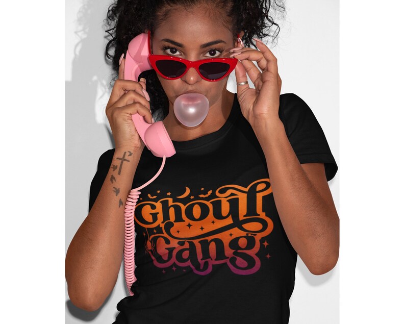 May include: A black t-shirt with an orange, yellow, and pink gradient design that says "Ghoul Gang" with stars and bats around the text.