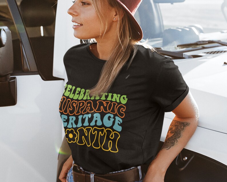 May include: A black t-shirt with a colorful graphic that says "Celebrating Hispanic Heritage Month" in a retro font. The graphic includes a yellow flower.
