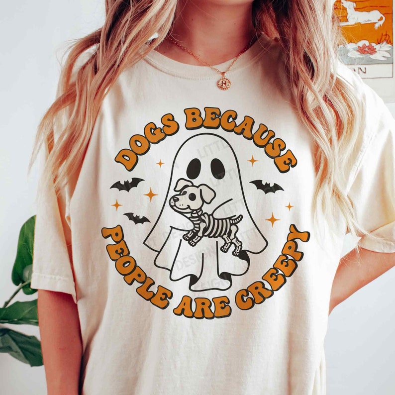 May include: A white t-shirt with a graphic design of a ghost holding a skeleton dog. The text around the graphic says "Dogs because people are creepy".