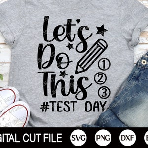 Peut inclure: Un t-shirt gris avec du texte noir qui dit "Let's Do This #Test Day". Le texte est dans une police d'écriture manuscrite et comprend un crayon, des étoiles et les chiffres 1, 2 et 3.