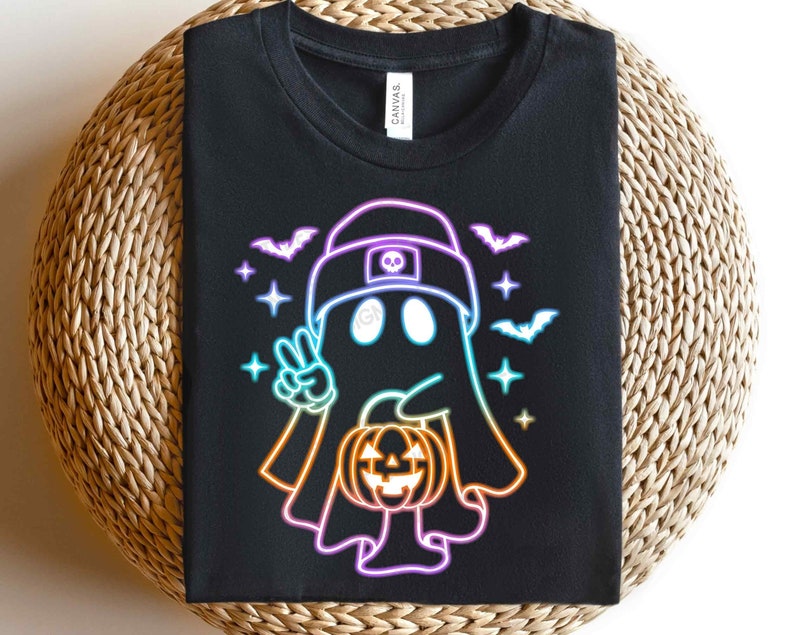 May include: Black t-shirt featuring a neon rainbow design of a ghost holding a jack-o'-lantern. The ghost is wearing a hat with a skull and crossbones.