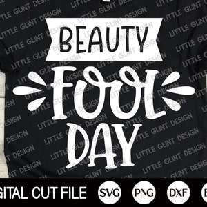 Op de afbeelding: Een zwart T-shirt met witte tekst die "Beauty Fool Day" luidt. De tekst is in een gestileerd lettertype en heeft een decoratieve versiering. Het shirt is een digitaal snijbestand en is beschikbaar in de formaten SVG, PNG, DXF en EPS.