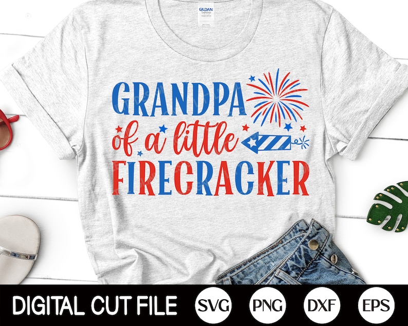 May include: A white t-shirt with red, white, and blue text that reads "Grandpa of a little firecracker". The text is surrounded by red, white, and blue stars and a firework graphic.
