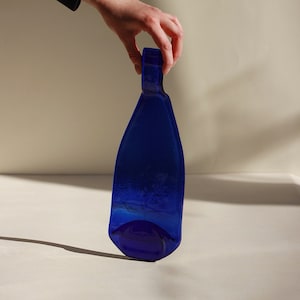 Op de afbeelding: Een kobaltblauwe glazen fles met een unieke vorm en een getextureerd oppervlak.