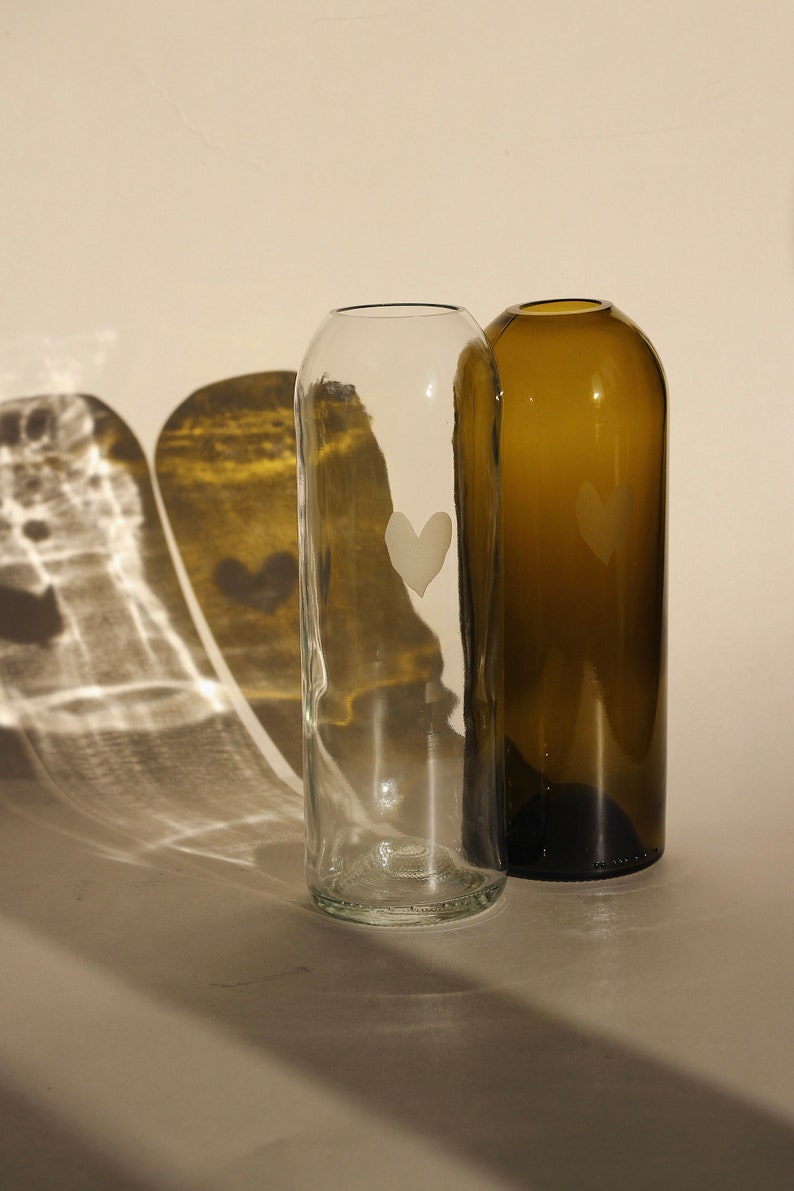 May include: Two glass vases, one clear and one brown, with a heart etched into the front of each.