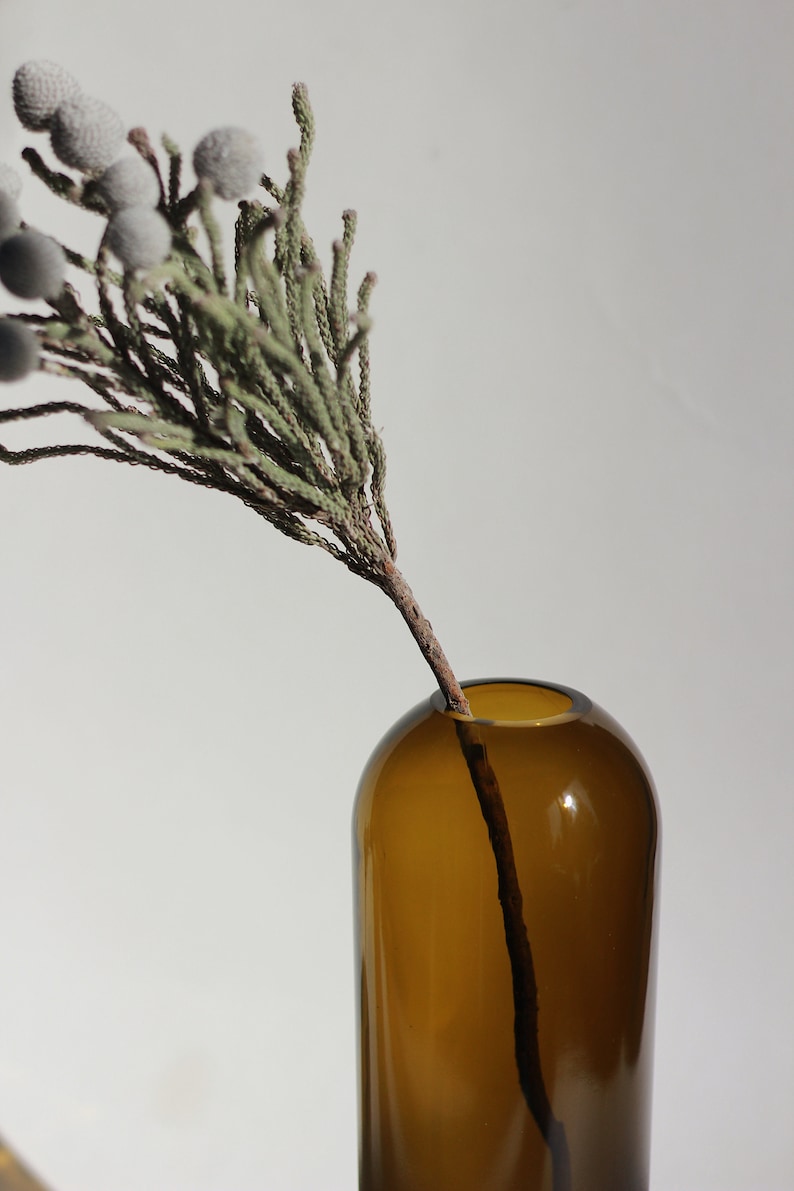 May include: A brown glass vase with a single sprig of dried greenery with small white berries.