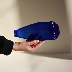May include: A hand holds a blue glass bottle, the bottle is slightly curved and has a rounded end.