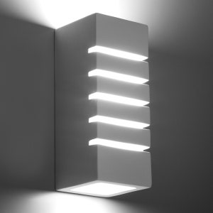 Op de afbeelding: Een witte, rechthoekige wandlamp met horizontale spleten die helder licht uitstralen. De armatuur heeft een vierkante basis en is op een grijze muur gemonteerd, wat een moderne, minimalistische uitstraling creëert.