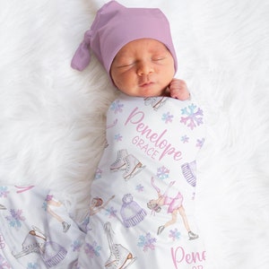 May include: A white swaddle blanket with a pink and purple ice skating theme. The blanket features a girl ice skating, snowflakes, and ice skates. The text "Penelope Grace" is written on the blanket.