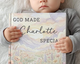Puede incluir: Un bebé dormido sostiene un libro titulado "GOD MADE Charlotte SPECIAL". La portada del libro presenta un paisaje de acuarela con montañas, flores y una puesta de sol. El bebé lleva una camiseta gris de manga larga.