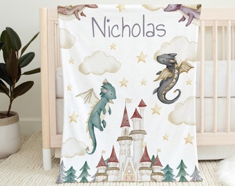 May include: A white baby blanket with a whimsical dragon and castle design. The blanket features two dragons flying in the sky with clouds and stars. The text "Nicholas" is printed in purple on the blanket.