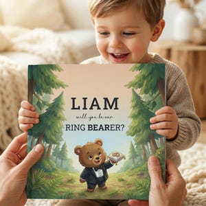 May include: A personalized book with the text "LIAM will you be our RING BEARER?" features a cartoon bear in a tuxedo holding a ring pillow. The cover has a forest scene with green trees and a light background.
