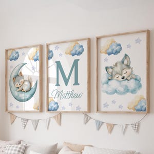 May include: Three framed watercolor prints with a nursery theme. One print features a sleeping wolf on a crescent moon, another has the letter "M" and the name "Matthew", and the third shows a sleeping wolf on a cloud. The prints have a light wood frame.