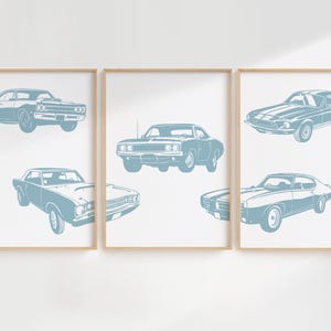 Pode incluir: Tr&ecirc;s impress&otilde;es emolduradas de carros musculares vintage azuis em silhueta em uma parede branca. Os carros s&atilde;o um Dodge Charger, um Ford Mustang e um Chevrolet Camaro.