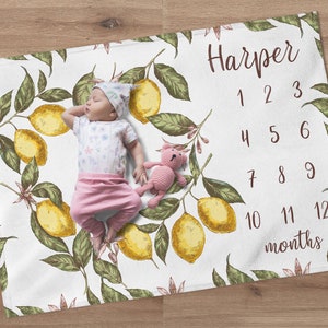 May include: A white baby blanket with a lemon print and numbers 1-12 for tracking a baby's growth. The blanket has the name "Harper" printed on it.