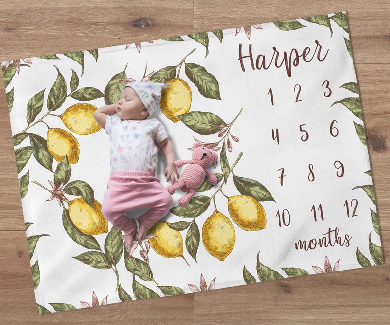 May include: A white baby blanket with a lemon print and numbers 1-12 for tracking a baby's growth. The blanket has the name "Harper" printed on it.