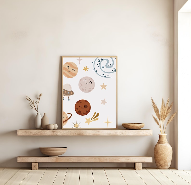 K&ouml;nnte beinhalten: Ein wei&szlig;er gerahmter Druck mit einer skurrilen Illustration von Planeten, Sternen und einer Galaxie. Die Planeten haben l&auml;chelnde Gesichter und sind in verschiedenen Farben, darunter Braun, Orange und Rosa. Die Sterne sind gelb und die Galaxie ist blau.
