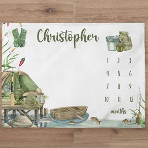 May include: A white baby blanket with a fishing theme. It features a green tent, a fishing rod, a life vest, a boat, and fish. The blanket also has a chart for tracking a baby's growth in months. The name "Christopher" is written at the top of the blanket.