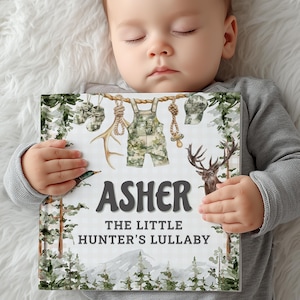 May include: A personalized children's book titled "Asher The Little Hunter's Lullaby." The cover features illustrations of hunting-themed items, including camouflage overalls, antlers, and a deer. The book is held by a baby.