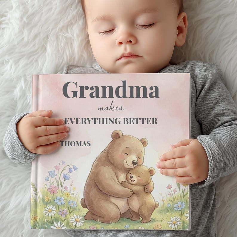 K&ouml;nnte beinhalten: Ein personalisiertes Buch mit dem Text "Oma macht ALLES BESSER" und dem Namen "Thomas". Das Cover zeigt eine Aquarellillustration eines B&auml;ren, der einen Babyb&auml;ren umarmt, umgeben von Blumen. Das Buch wird von einem Baby gehalten.