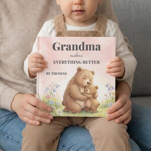 K&ouml;nnte beinhalten: Ein Kinderbuch mit rosa Einband, gehalten von einem Kind. Auf dem Einband steht "Oma macht ALLES BESSER" mit dem Namen "Thomas" darunter. Die Illustration zeigt einen Mutterb&auml;ren, der einen Babyb&auml;ren umarmt.