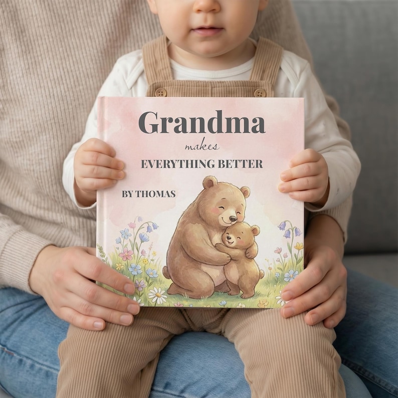 K&ouml;nnte beinhalten: Ein Kinderbuch mit rosa Einband, gehalten von einem Kind. Auf dem Einband steht "Oma macht ALLES BESSER" mit dem Namen "Thomas" darunter. Die Illustration zeigt einen Mutterb&auml;ren, der einen Babyb&auml;ren umarmt.