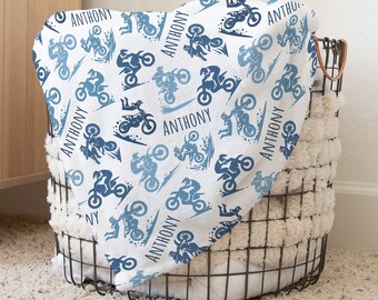 May include: A white baby blanket with a blue and white pattern of dirt bikes and the name "ANTHONY" repeated throughout.