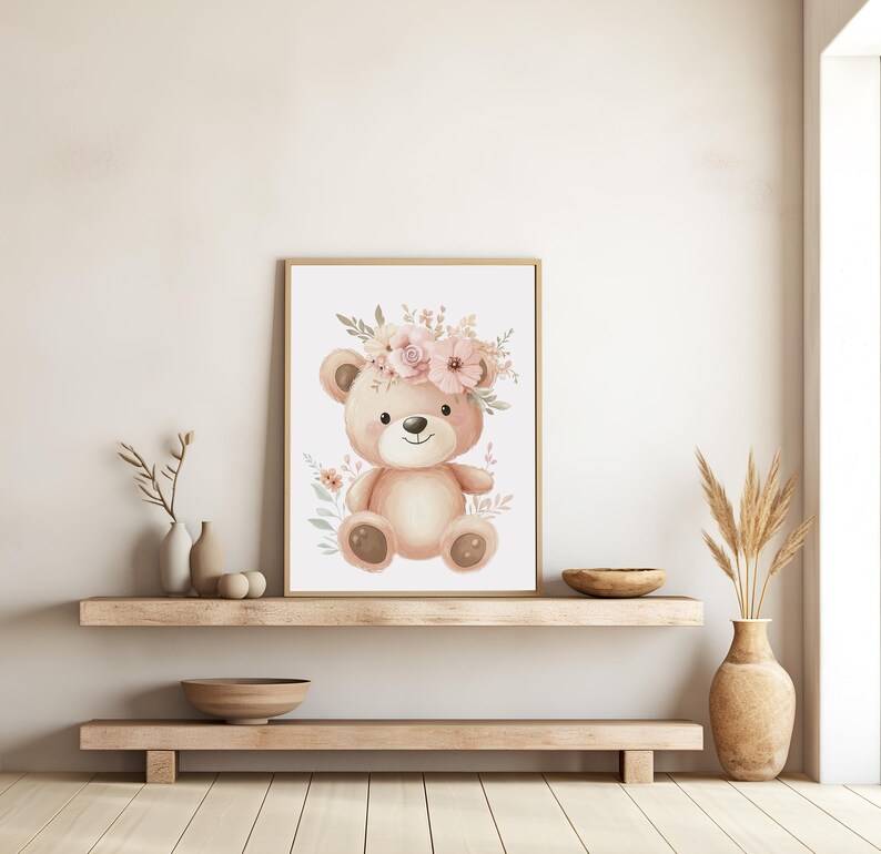 May include: A framed watercolor print of a teddy bear wearing a floral crown. The bear is light brown with a smiling face and sits against a white background. Soft pink and green floral accents surround the bear, creating a gentle, nursery-themed artwork.