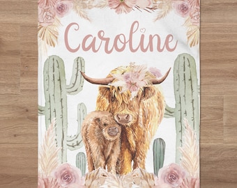 May include: A watercolor illustration of a Highland cow and calf with a floral crown on the cow's head. The background features cacti, pampas grass, and pink flowers. The text "Caroline" is written in pink script above the cow.