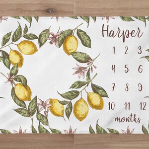 May include: A white baby milestone blanket with a lemon branch design. The blanket has the name "Harper" and numbers 1 through 12 to track a baby's growth.