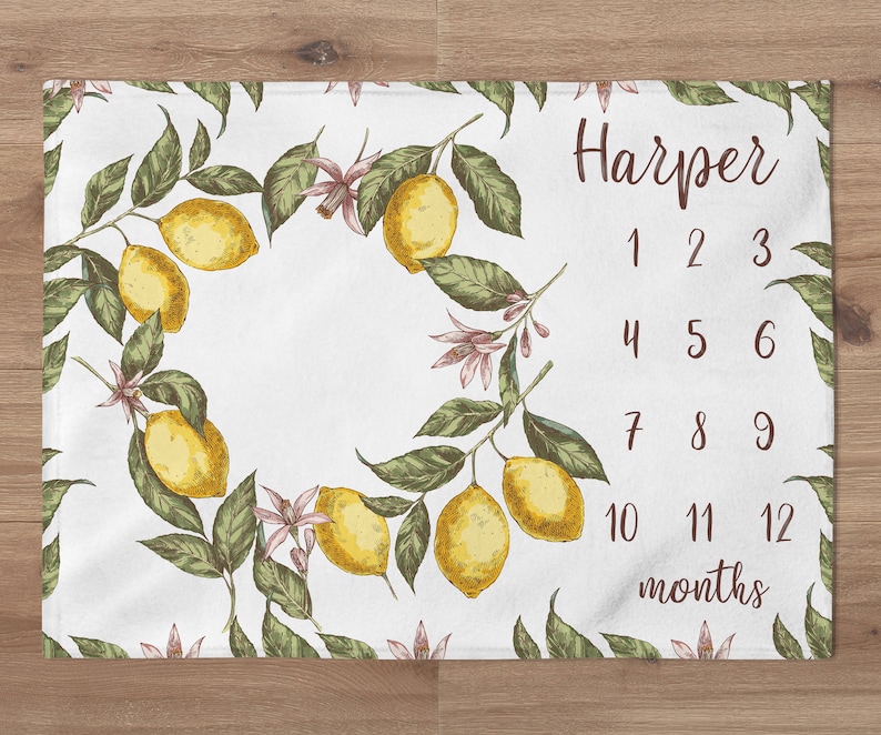 May include: A white baby milestone blanket with a lemon branch design. The blanket has the name "Harper" and numbers 1 through 12 to track a baby's growth.