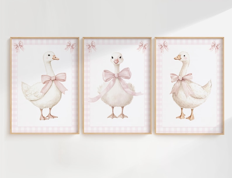 K&ouml;nnte beinhalten: Set aus drei gerahmten Kunstdrucken mit Aquarellillustrationen von wei&szlig;en G&auml;nsen mit rosa Schleifen. Jede Gans ist vor einem rosa Vichy-Hintergrund platziert und in hellem Holz gerahmt. Dekorative Schleifen befinden sich oben an jedem Rahmen.