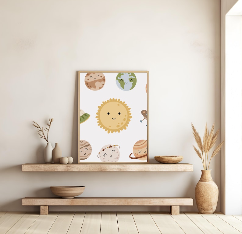 K&ouml;nnte beinhalten: Ein wei&szlig;es Poster mit einer Cartoon-Illustration einer gelben Sonne und Planeten mit l&auml;chelnden Gesichtern. Die Planeten sind braun, gr&uuml;n, blau und orange. Das Poster ist in einem d&uuml;nnen braunen Rahmen gerahmt und h&auml;ngt an einer wei&szlig;en Wand.