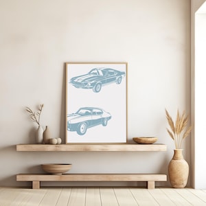 Pode incluir: Uma impress&atilde;o emoldurada com uma silhueta azul de dois carros cl&aacute;ssicos. Os carros s&atilde;o um Ford Mustang e um Pontiac GTO. A impress&atilde;o est&aacute; pendurada em uma parede branca acima de uma prateleira de madeira.