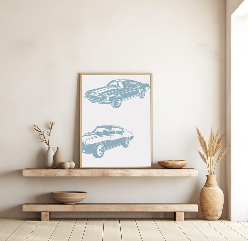 Pode incluir: Uma impress&atilde;o emoldurada com uma silhueta azul de dois carros cl&aacute;ssicos. Os carros s&atilde;o um Ford Mustang e um Pontiac GTO. A impress&atilde;o est&aacute; pendurada em uma parede branca acima de uma prateleira de madeira.