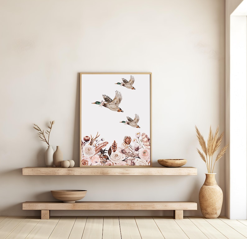 Peut inclure: Une impression d'art encadr&eacute;e repr&eacute;sentant trois canards en vol sur fond blanc. Le bas de l'impression pr&eacute;sente un arrangement floral dans les tons de rose, marron et blanc. Le cadre est de couleur marron clair.