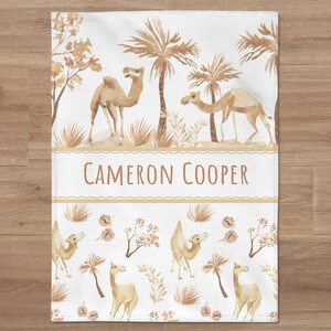 May include: A white personalized baby blanket with a camel and palm tree design. The blanket has the name "CAMERON COOPER" printed on it.