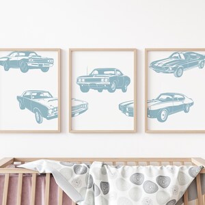 Pode incluir: Tr&ecirc;s impress&otilde;es emolduradas de carros musculares azuis em silhueta em uma parede branca. As impress&otilde;es est&atilde;o em um ambiente de ber&ccedil;&aacute;rio com um ber&ccedil;o em primeiro plano.