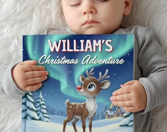 May include: A baby sleeps while holding a children's book titled "WILLIAM'S Christmas Adventure." The book cover features a cartoon reindeer in a snowy landscape with a green and blue aurora borealis background. The baby is wearing a gray long-sleeved shirt.