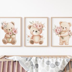 May include: Set of three framed watercolor prints featuring adorable teddy bears. Each bear is depicted with a floral crown or holding a bouquet of pink flowers. The artwork has a soft, pastel color palette, perfect for a nursery or children's room.