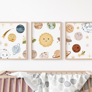 K&ouml;nnte beinhalten: Drei gerahmte Drucke mit wei&szlig;em Hintergrund und bunten Illustrationen von Planeten und Sternen. Die Planeten haben l&auml;chelnde Gesichter und sind von Sternen und Kometen umgeben.