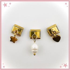 May include: Three gold-toned modular bracelet links, each featuring a rectangular base. The left link has a dangling star charm, the center link features a dangling white pearl-like bead, and the right link includes a dangling heart-shaped charm.