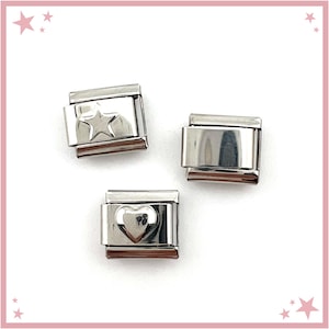 May include: Three rectangular stainless steel modular bracelet links. One link features a raised five-pointed star, one link features a raised heart shape, and one link has a plain, smooth, polished silver-tone surface with no additional design.