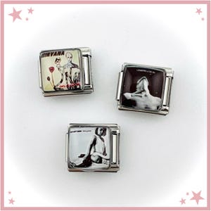 May include: Three silver charm bracelets, each with a square image of Nirvana album art. The top left charm displays the "Nevermind" album cover, the top right charm has a monochrome image, and the bottom charm shows a black and white image.