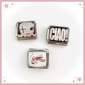 May include: Three square charms with silver-coloured metal frames. One charm features a face with a cross over one eye. Another charm has the word "CIAO!" in white on a black background. The third charm shows ballet shoes.