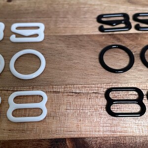 May include: A set of white and black bra strap adjusters. The set includes two pairs of white and two pairs of black adjusters. The adjusters are made of plastic and have a smooth finish.