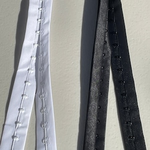 May include: Two strips of white and black fabric with rows of metal hooks and eyes for sewing onto garments.