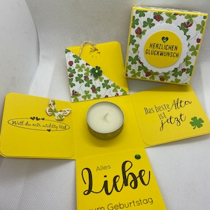 Könnte beinhalten: Eine gelbe und weiße Geschenkbox mit einem grünen Kleeblatt-Design. Die Box ist geöffnet und enthält eine kleine Kerze. Die Box hat den Text "Herzlichen Glückwunsch" und "Das beste Alter ist jetzt" darauf. Die Box hat auch den Text "Weil du mir wichtig bist" und "Alles Liebe zum Geburtstag" darauf.